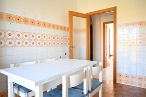 Ein Essbereich mit einem weißen Tisch und Stühlen, einer gefliesten Spritzschutzwand mit orange-weißen Mustern und einer Holztür, die in einen anderen Raum führt.