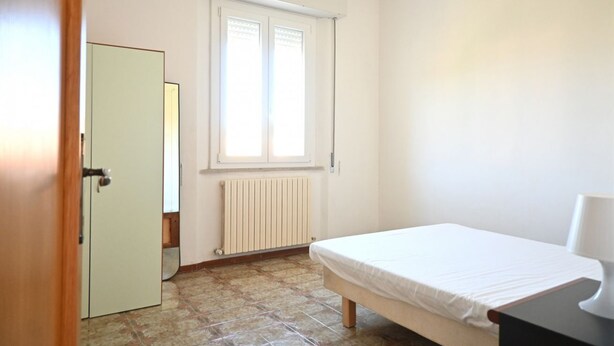 Un dormitorio con cama, radiador, ventana y puerta.