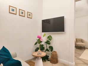 Ein Wohnzimmer mit einem an der Wand montierten Flachbildfernseher, einem kleinen runden Tisch mit einer Vase und einer Topfpflanze.