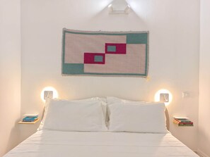 A bed with white bedding, a wall hanging with geometric patterns, and bedside lamps. - Piccola Dimora in Palazzo Cadello Rossi (Cagliari)