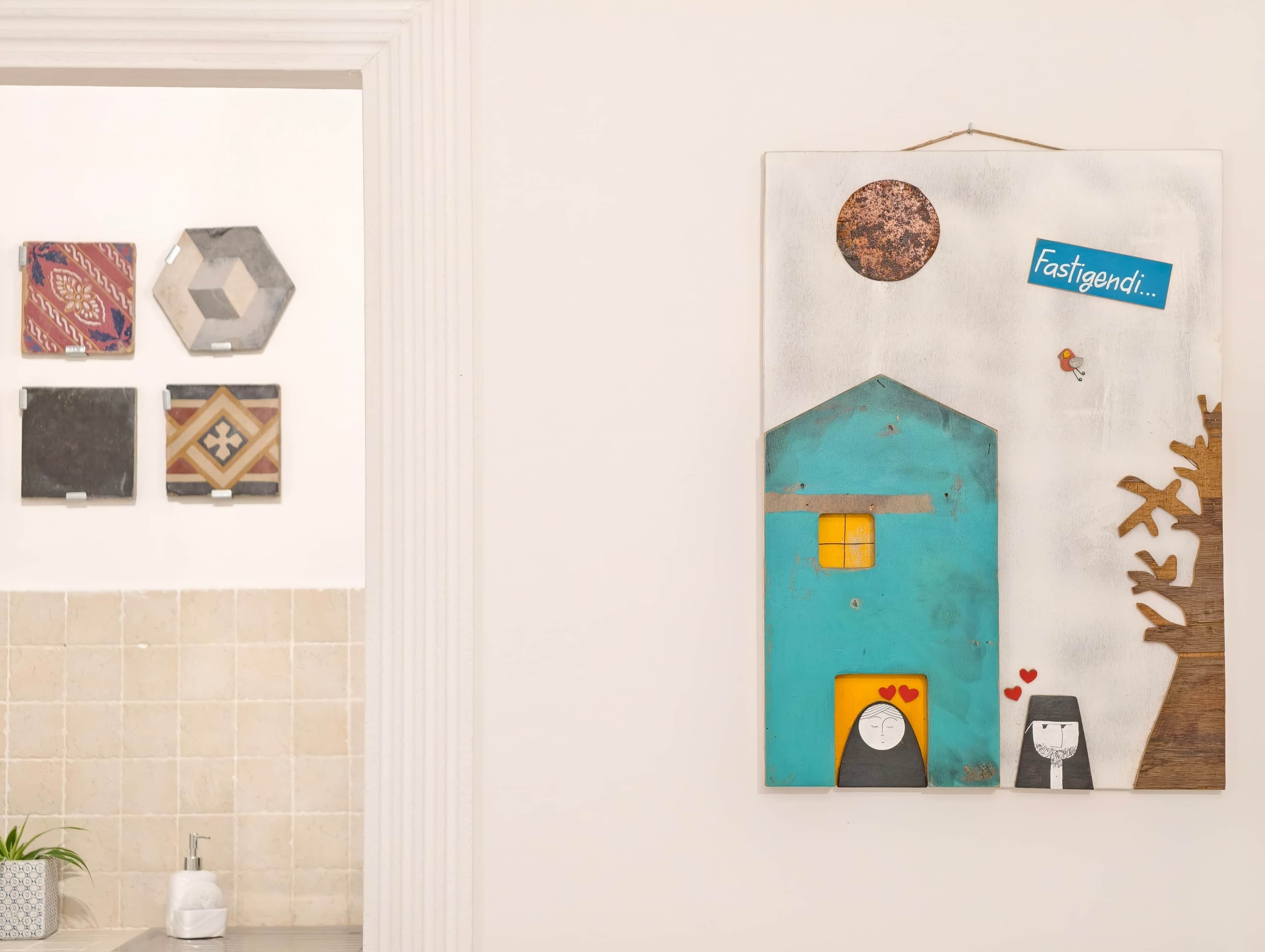 A wall with various tiles and a large artwork depicting a house with a person and a tree.