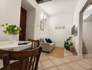A compact living space with a dining area, a sofa, and a television mounted on the wall. - Piccola Dimora in Palazzo Cadello Rossi (Cagliari)