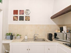 A kitchen with a sink, countertop, and various items like a coffee maker, toaster, and decorative tiles. - Piccola Dimora in Palazzo Cadello Rossi (Cagliari)