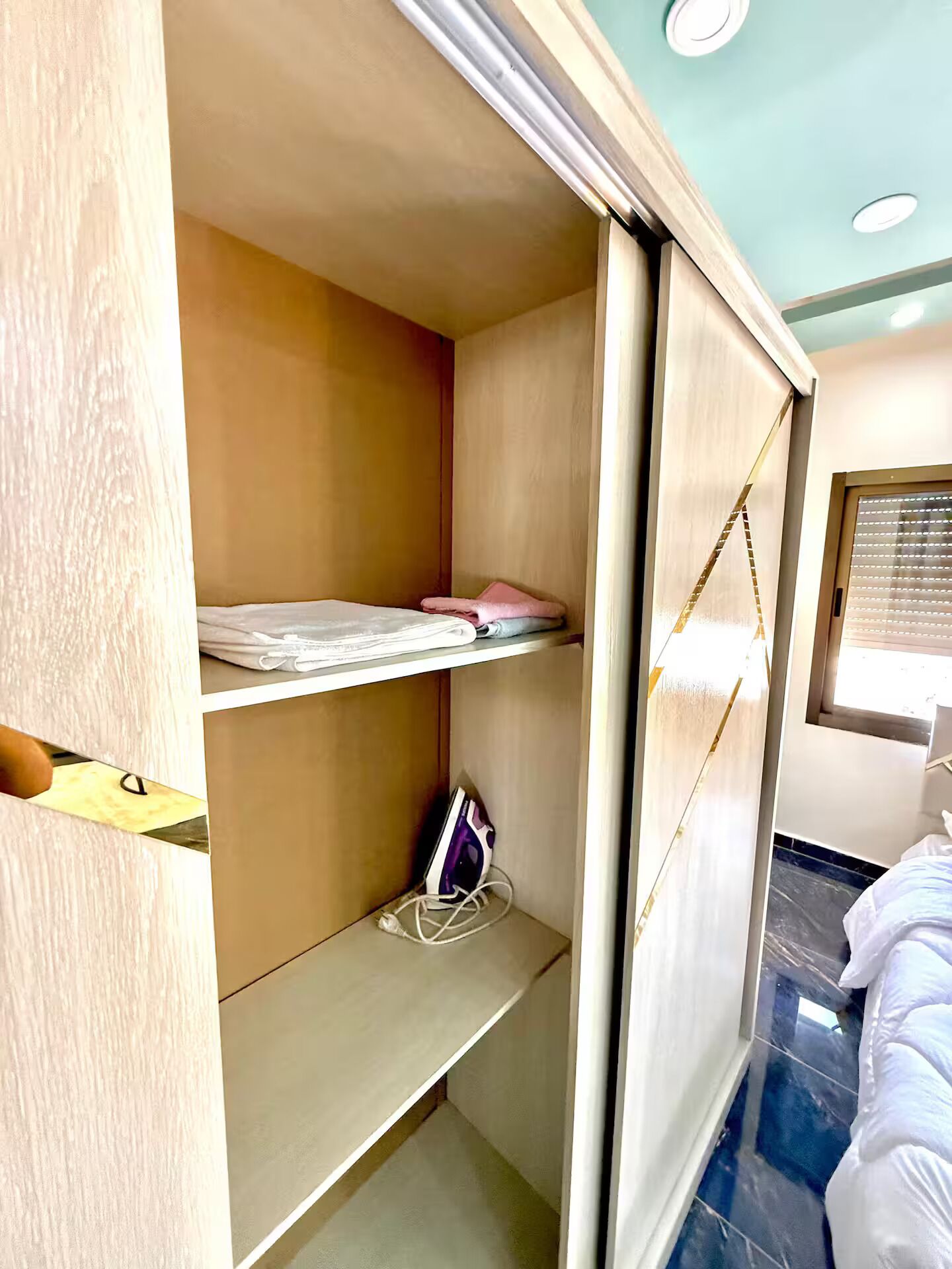A room with a wardrobe, a bed, and a window with blinds.