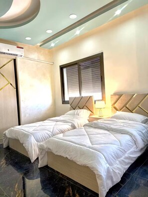 A hotel room with a bed, bedside tables, a window with blinds, and a ceiling light fixture. - Luxury 2 Bedroom Apartment (Amman)