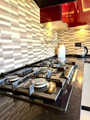 A modern kitchen with a gas stove, a coffee maker, and a red cabinet. - Luxury 2 Bedroom Apartment (Amman)
