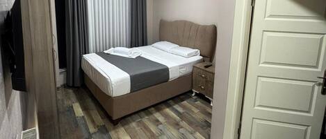 A hotel room with a bed, a bedside table, a TV, a radiator, and a door.