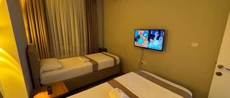 Una camera d'albergo con due letti, una televisione a parete e una finestra con tende.
