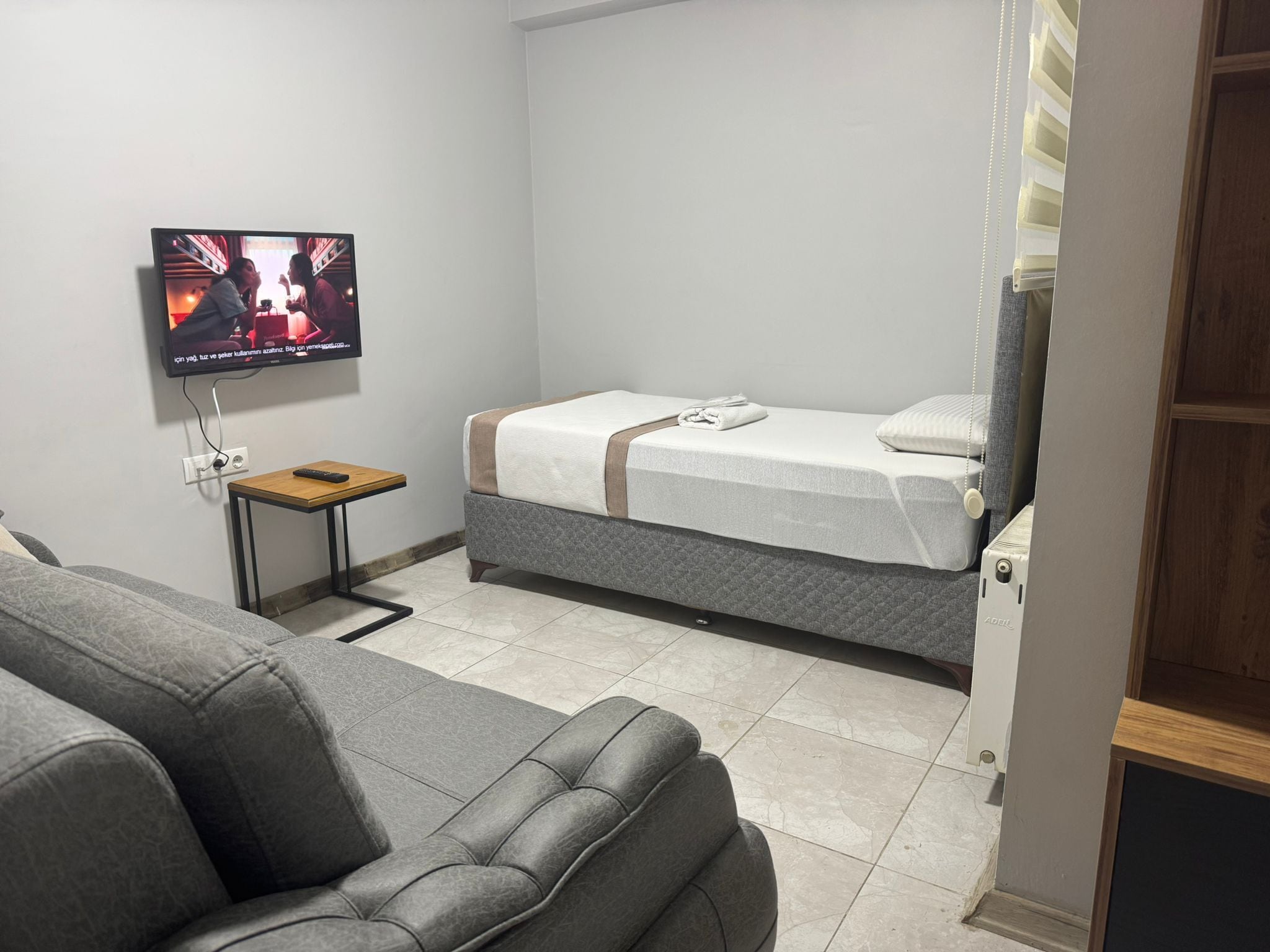 A hotel room with a bed, a television mounted on the wall, a small table, and a sofa.