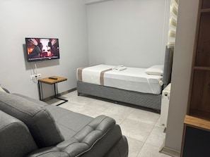 Une chambre d’hôtel avec un lit, un téléviseur fixé au mur, une petite table et un canapé.