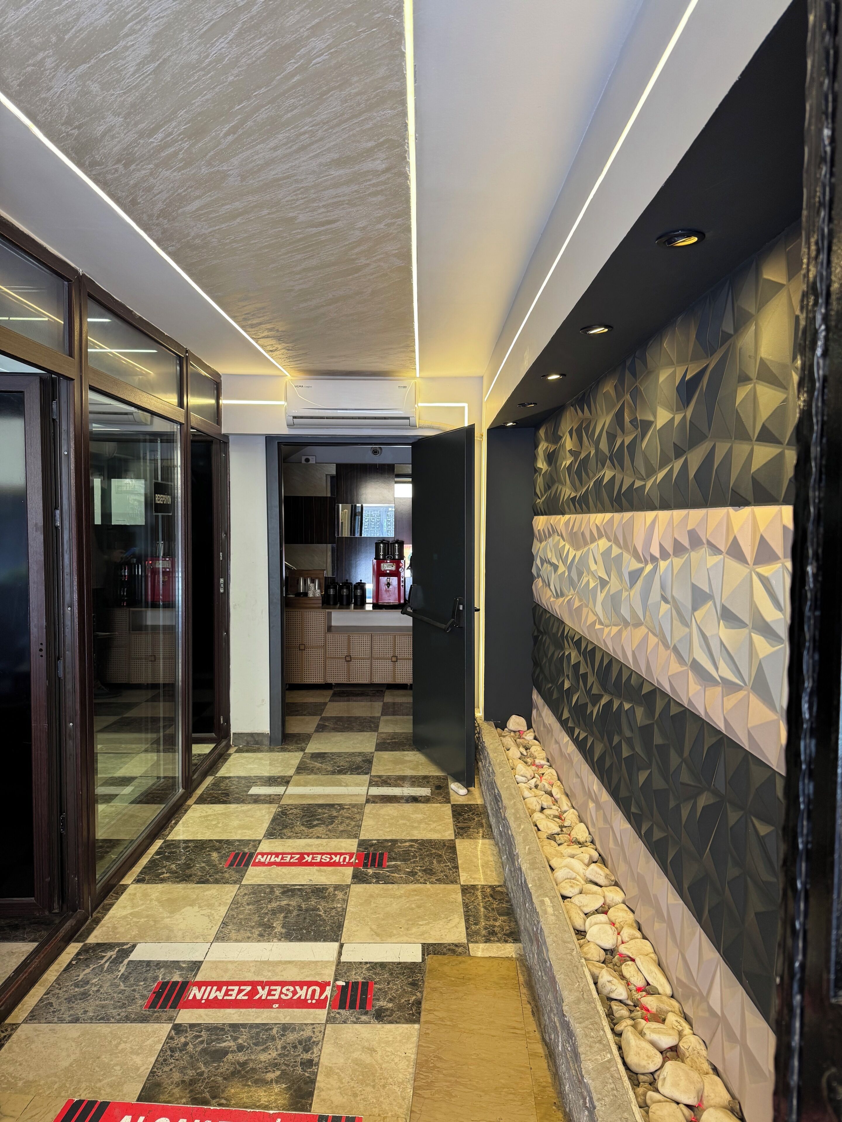 A modern hallway with a checkered floor, a reception area, and a kitchen visible in the background.