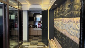 A modern hallway with a checkered floor, a reception area, and a kitchen visible in the background.
