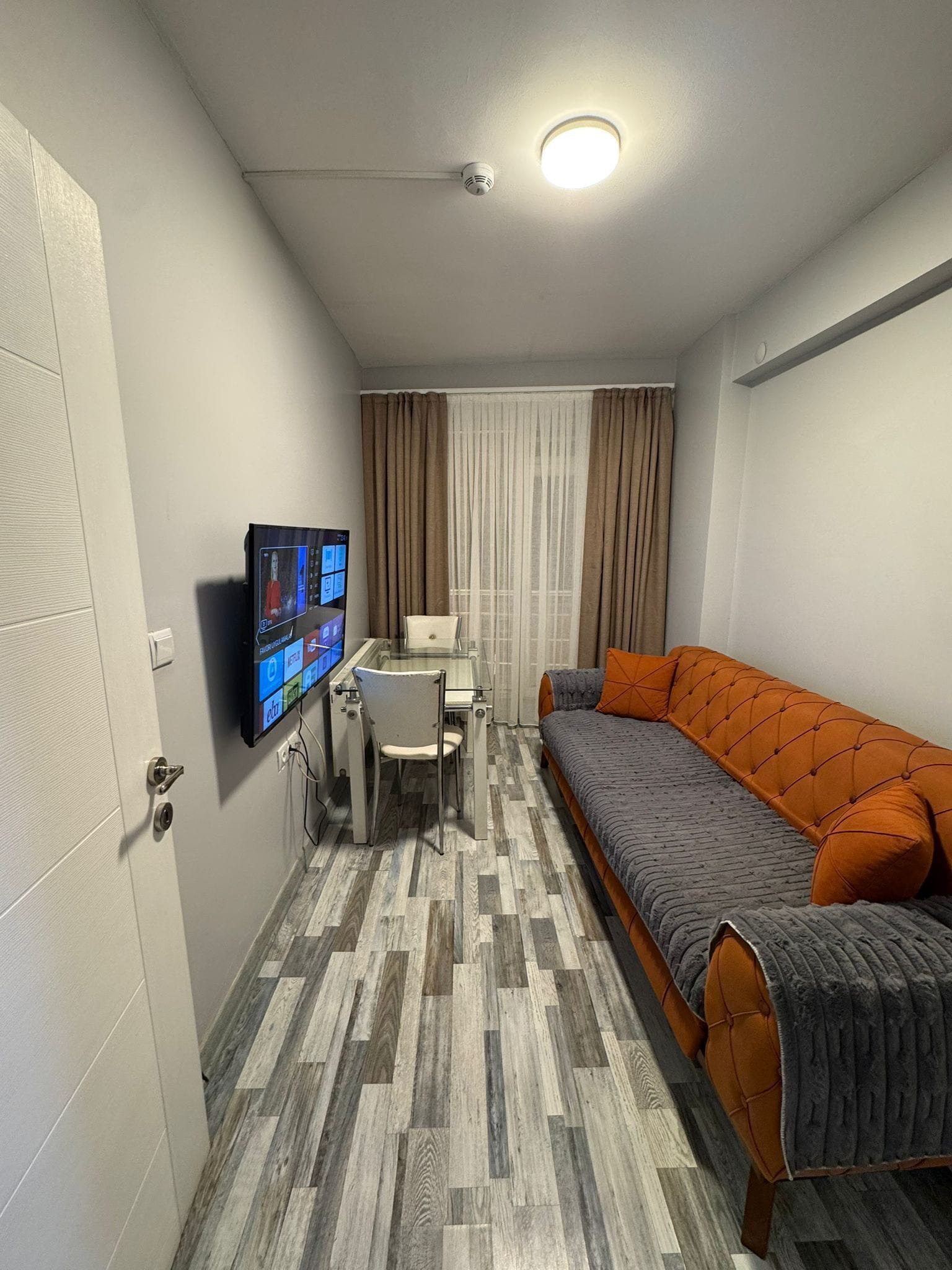 A compact room with a bed, a desk with a computer, and a television mounted on the wall.