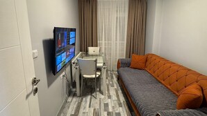 A compact room with a bed, a desk with a computer, and a television mounted on the wall.