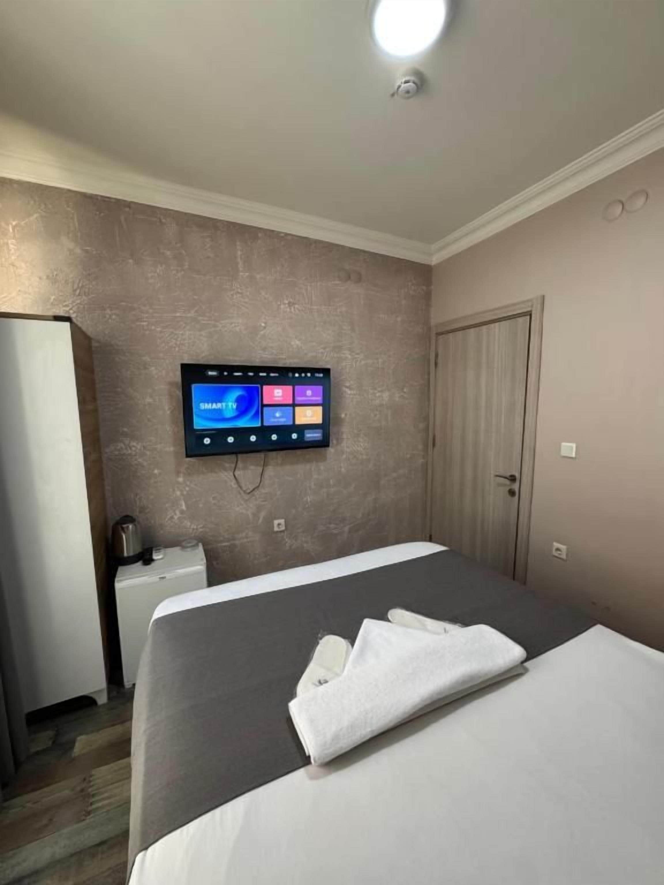 A hotel room with a bed, a flat-screen TV mounted on the wall, a bedside table, and a door.