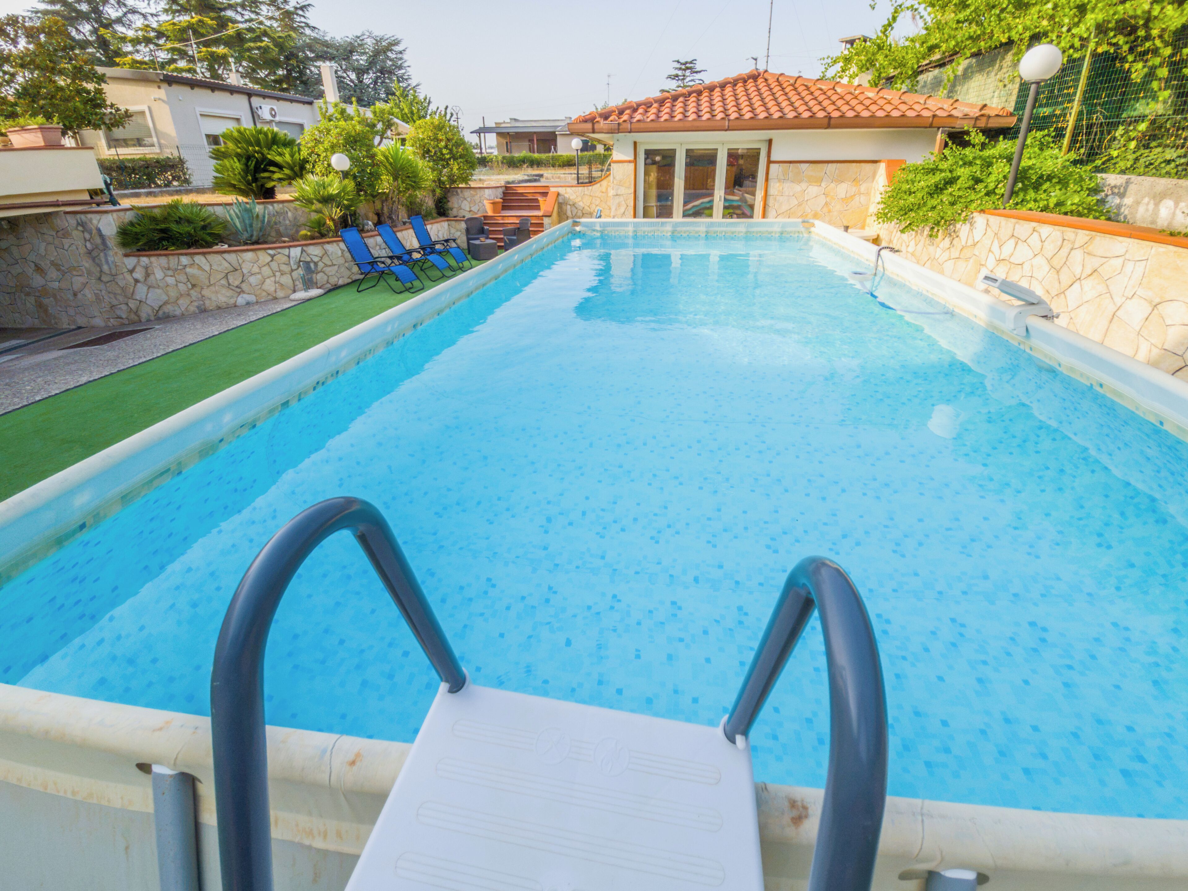 Una piscina con trampolín, rodeada por un muro de piedra y vegetación.
