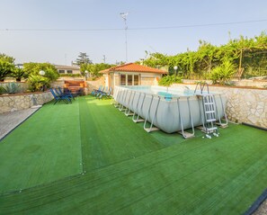 Ein Pool im Freien mit Steinmauer, umgeben von Kunstgrün, und mit mehreren Liegestühlen ausgestattet.