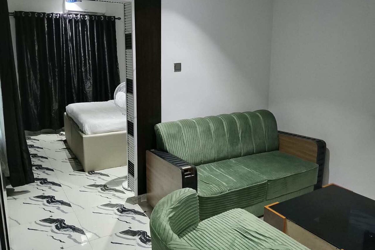 Una habitación con cama, sofá verde, una mesita y un espejo.
