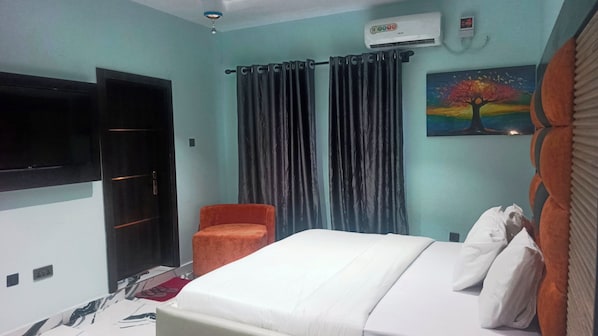 A hotel room with a bed, a chair, a painting, curtains, and an air conditioning unit.