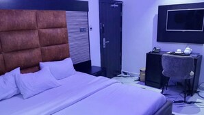 A hotel room with a large bed, a desk with a chair, a television, and a door. - ERATON HOTEL (Warri)