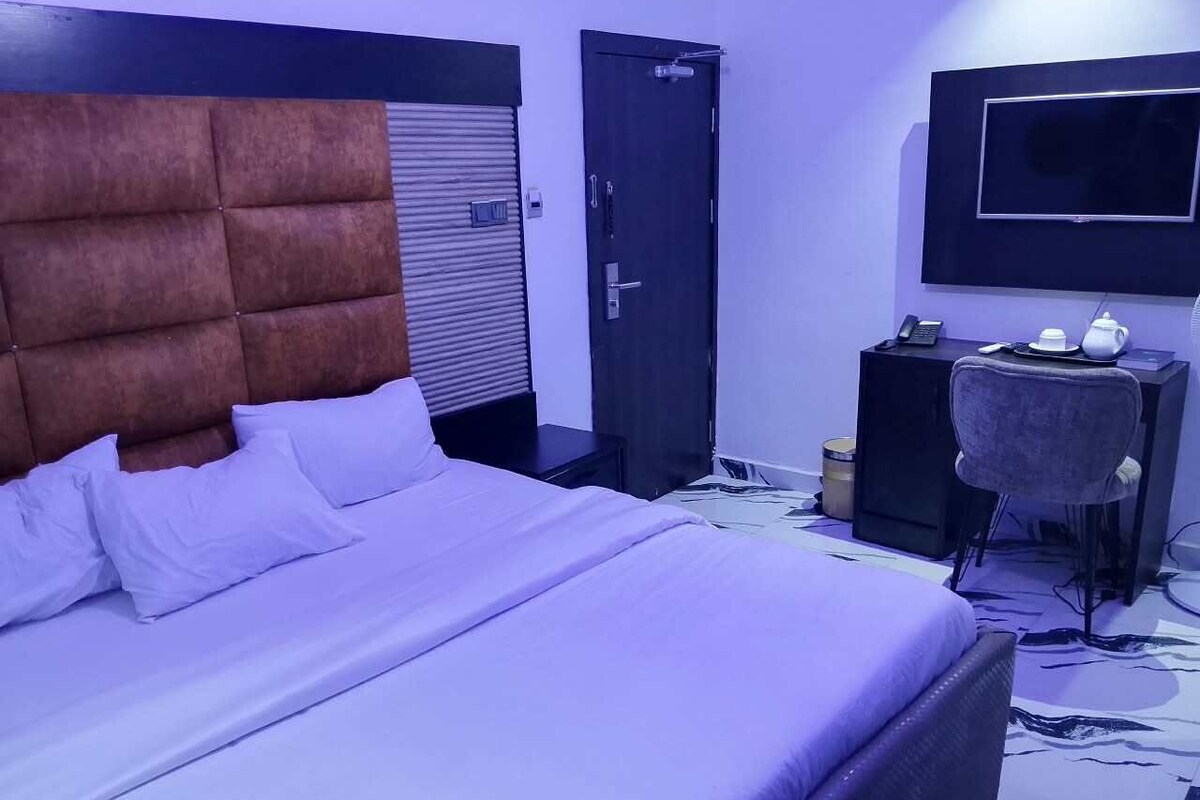Una habitación de hotel con una cama grande, un escritorio con silla, televisión y puerta.