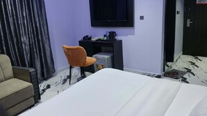 Hotellihuone, jossa on sänky, työpöytä tietokoneella, tuoli, televisio ja ovi, jossa on tupakointikieltokyltti.