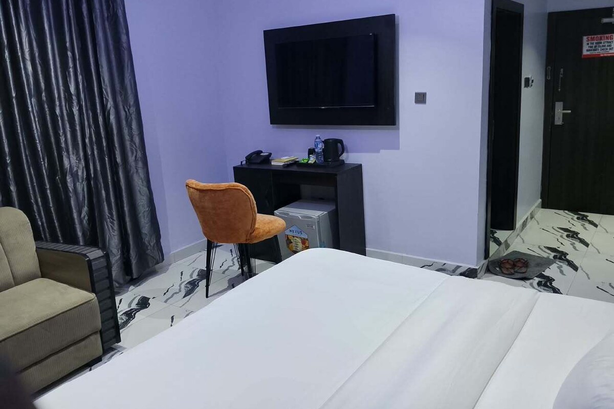 Habitación de hotel con cama, escritorio con computadora, silla, televisor y puerta con un letrero de no fumar.