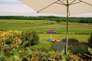 A grassy outdoor area with a large umbrella, a red and white inflatable toy, and a play structure. - La Cabane; a comfortable, detached gîte for two with a spacious terrace (Les Bois d'Anjou)
