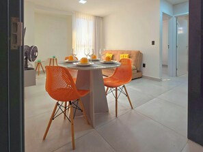 Ein Essbereich mit einem runden Tisch, zwei orangefarbenen Stühlen und einer Couch im Hintergrund.