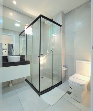 Ein modernes Badezimmer mit einer in Glas abgeschlossenen Dusche, einer weißen Toilette und einer schwarzen Ablage mit Waschbecken.