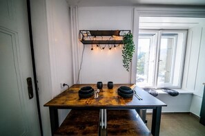 A dining table with four bowls and cutlery, a hanging plant, and a shelf with lights. - Premium Stay at March 15 Sq: Promenade, River Views & Top Comfort – 231 (Budapest)