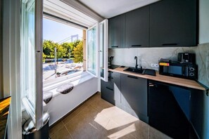 Eine kleine Küche mit Fenster, Spüle, Mikrowelle und kleinem Kühlschrank.