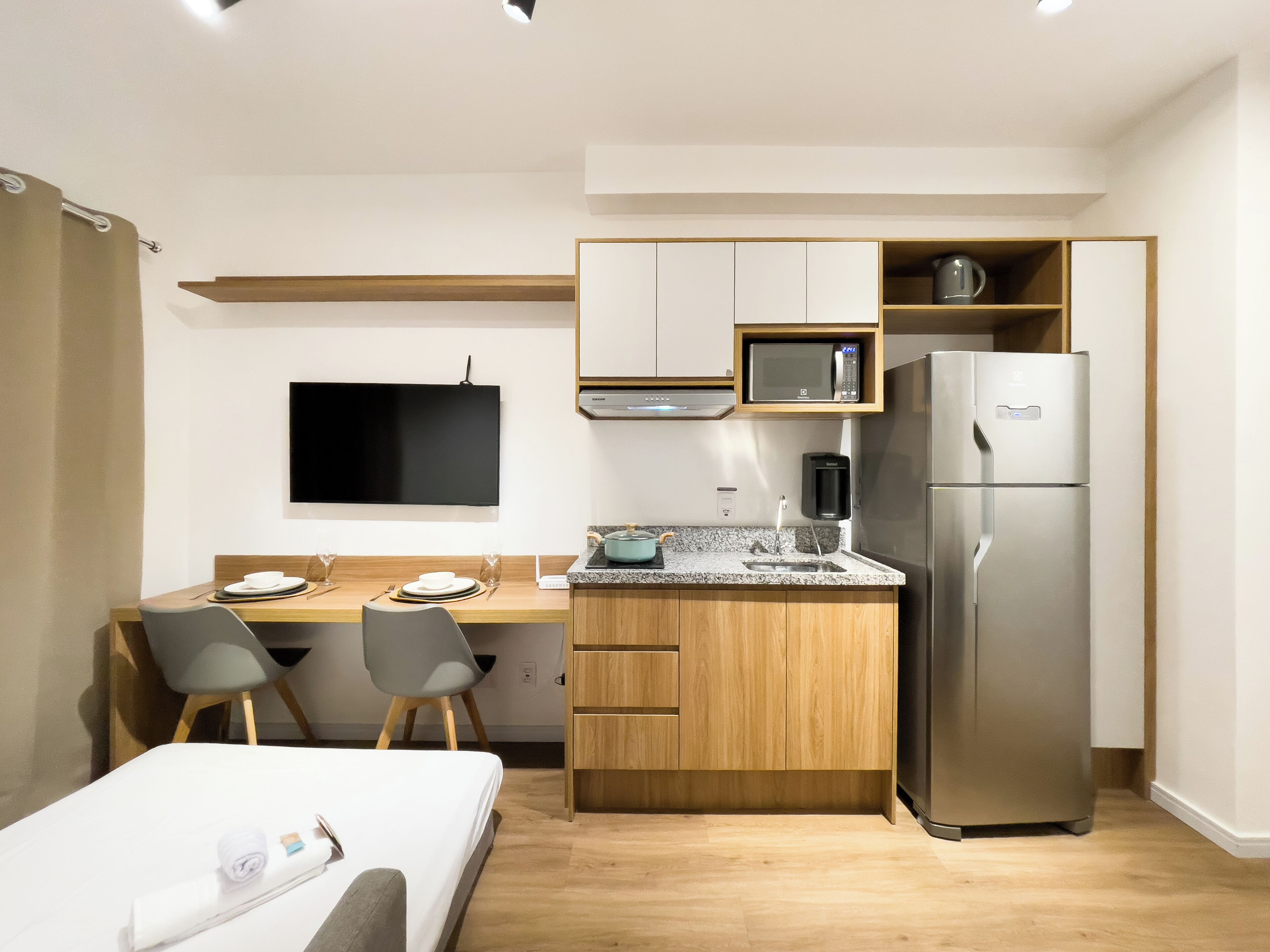 Habitación de hotel compacta con kitchenette, cama, escritorio con sillas y televisión de pantalla plana.