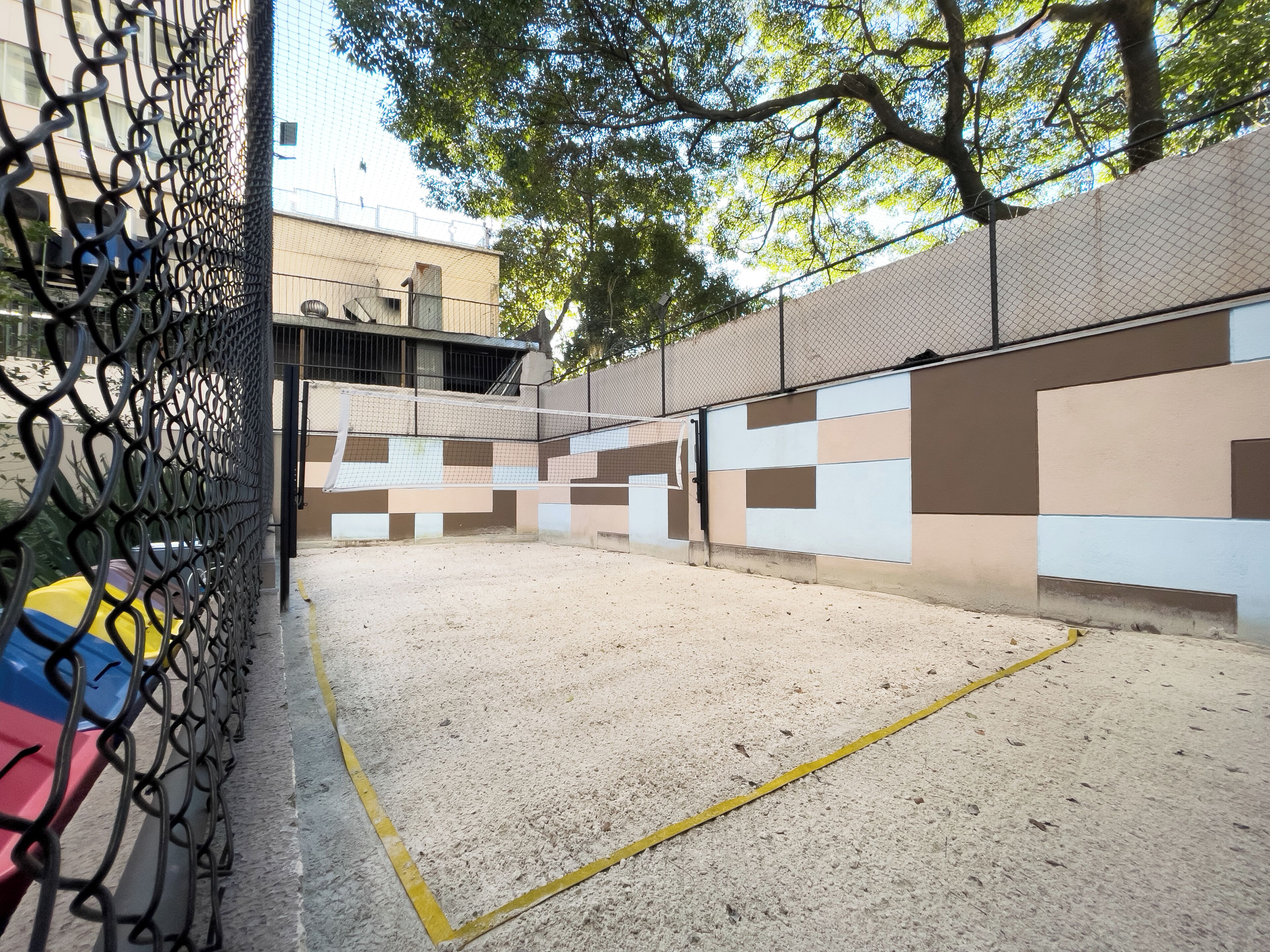 Una cancha de tenis interior con cerca de malla metálica, red y pared con diseño geométrico.
