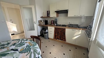 Een kleine keuken met witte kastjes, een gasfornuis en een koffiezetapparaat.