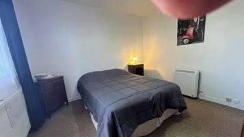 Een slaapkamer met een bed, nachtkastje, lamp en radiator.