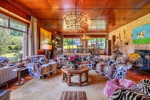 Ein geräumiges Wohnzimmer mit einer großen Holzbalkendecke, einer Kristallleuchtre und Blick ins Freie.