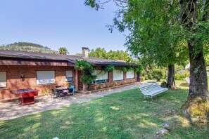 Ein Backsteinhaus mit überdachter Terrasse, Sitzgelegenheiten im Freien und einem Baum.