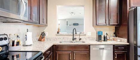 A kitchen with dark wood cabinets, a stainless steel refrigerator, a microwave, and a granite countertop.