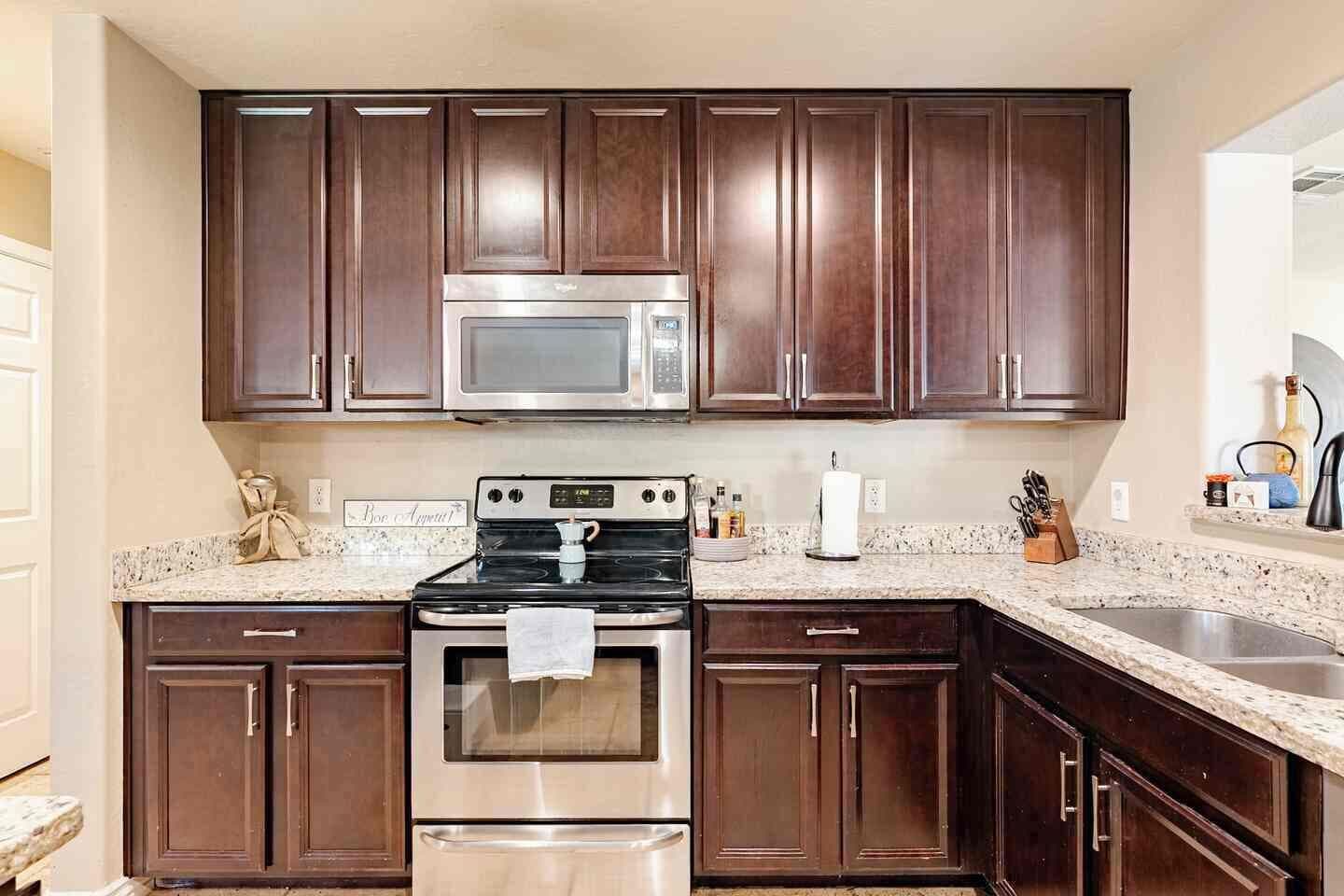 A kitchen with dark wooden cabinets, stainless steel appliances, granite countertops, and a built-in microwave.