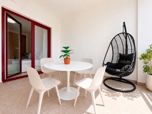 A dining area with a round table, white chairs, a hanging chair, and a potted plant. - Apartment Praia Rocha | Pool | Modern Vogue (Portimão)