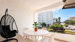Ein Balkon mit rundem Tisch, weißen Stühlen, einer Hängematte und einem Blumentopf.