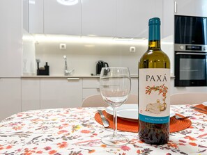 Eine Flasche PAXÁ Sauvignon Blanc auf einem Tisch mit einer blumigen Tischdecke, ein Weinglas und eine Küche im Hintergrund.