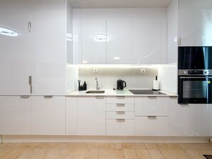 A modern kitchen with white cabinetry, a stainless steel sink, a black countertop, and a built-in oven. - Apartment Praia Rocha | Pool | Modern Vogue (Portimão)