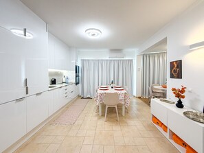 Eine moderne Küche mit weißen Schränken, ein Essbereich mit Tisch für zwei Personen und eine Wohnbereich mit Sofa und Couchtisch.