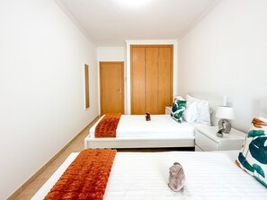 Et hotelværelse med to senge, en træskab, et sengebord med lampe og et spejl på væggen.