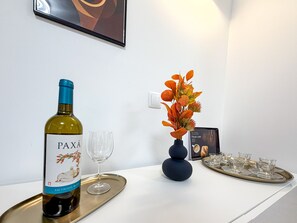 A bottle of PAXÁ Sauvignon Blanc on a tray with a wine glass, a decorative vase with autumn leaves, and a tray with glasses and a menu on a white table. - Apartment Praia Rocha | Pool | Modern Vogue (Portimão)