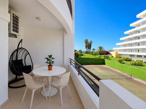 A balcony with a white table and chairs, a hanging chair, and a potted plant. - Apartment Praia Rocha | Pool | Modern Vogue (Portimão)