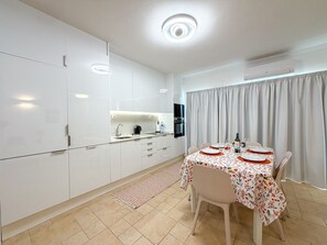 A modern kitchen with white cabinetry, a built-in oven, and a dining area with a table set for two. - Apartment Praia Rocha | Pool | Modern Vogue (Portimão)