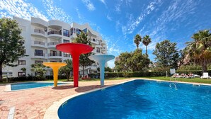 Ein Pool mit modernem Design, umgeben von einer angelegten Grünfläche mit Palmen und einem mehrstöckigen Gebäude im Hintergrund.